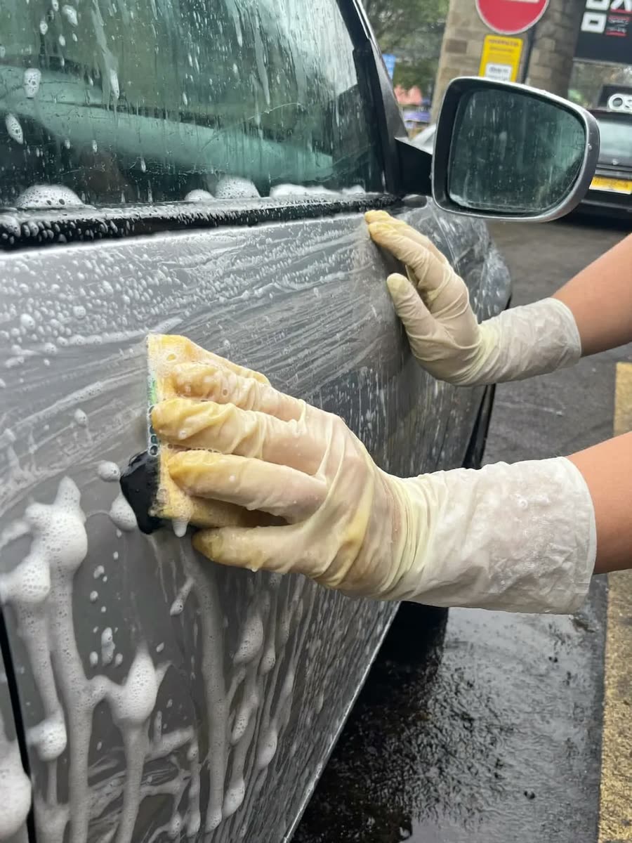 Hands washing a soapy car panel by hand