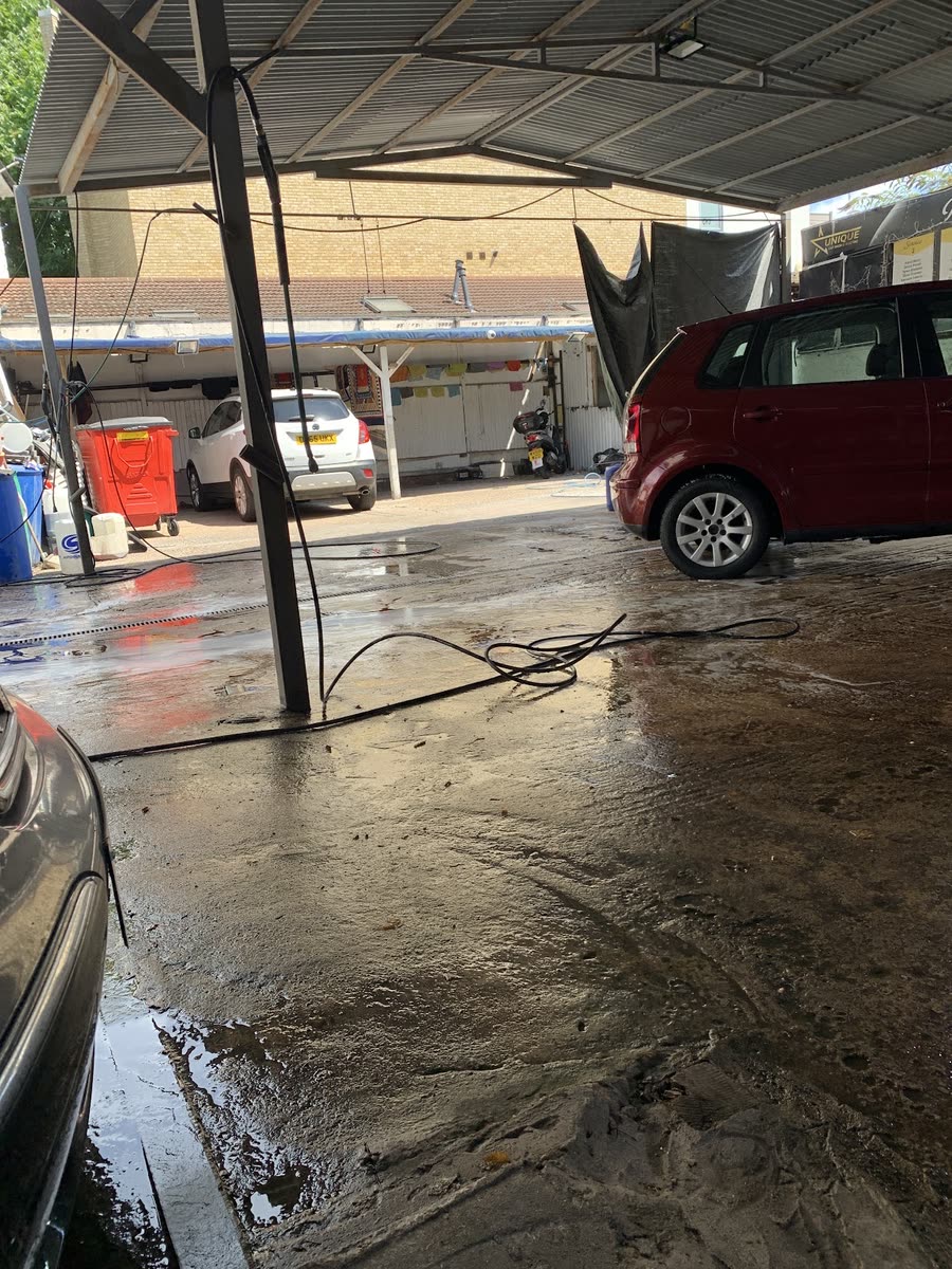 Inside the covered wash bay, hoses across the wet concrete floor with cars under the corrugated canopy